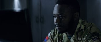 Movie still from “Eye in the Sky” (2015), directed by Gavin Hood – A man in a military uniform looking to his left; Close Up shot, Over the shoulder angle