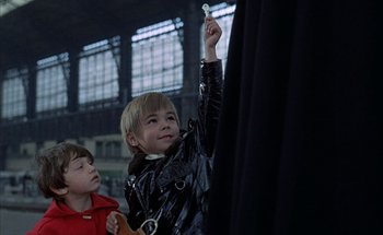 Movie still from “F for Fake” (1973), directed by François Reichenbach – A young boy holding up a piece of paper in front of another young boy; Medium shot, Low angle