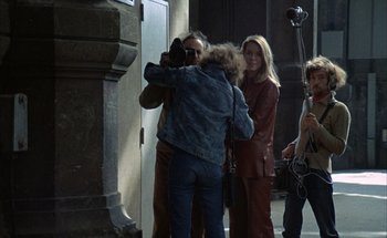 Movie still from “F for Fake” (1973), directed by François Reichenbach – A group of people standing next to each other in a room; Wide shot, Over the shoulder angle