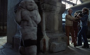 Movie still from “F for Fake” (1973), directed by François Reichenbach – A person standing next to a stone pillar; Medium shot, Over the shoulder angle