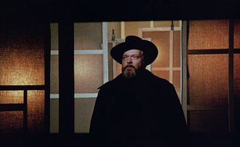 Movie still from “F for Fake” (1973), directed by François Reichenbach – A man with a long beard wearing a black hat; Medium shot, Low angle