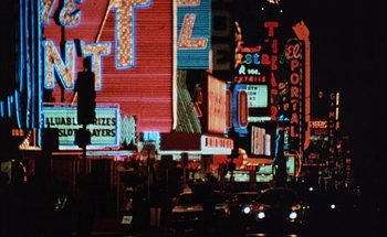 Movie still from “F for Fake” (1973), directed by François Reichenbach – A view of a city street at night with neon lights; Extreme Wide shot, High angle