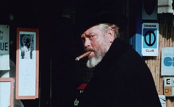 Movie still from “F for Fake” (1973), directed by François Reichenbach – An old man with a beard and a hat is smoking a cigar; Medium shot, Low angle
