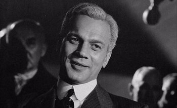 Movie still from “F for Fake” (1973), directed by François Reichenbach – Black and white photograph of a man in a suit and tie; Close Up shot, Low angle