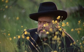 Movie still from “F for Fake” (1973), directed by François Reichenbach – An older man wearing a black hat in a field of yellow flowers; Close Up shot, Low angle