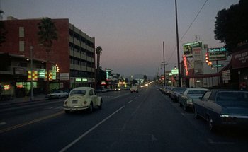 Movie still from “F for Fake” (1973), directed by François Reichenbach – Cars driving down a street at dusk in a city; Extreme Wide shot, High angle