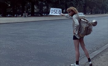 Movie still from “F for Fake” (1973), directed by François Reichenbach – A person standing on the side of the road holding a sign; Wide shot, High angle