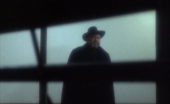 Movie still from “F for Fake” (1973), directed by François Reichenbach – A man wearing a black hat standing in front of a window; Close Up shot, Low angle