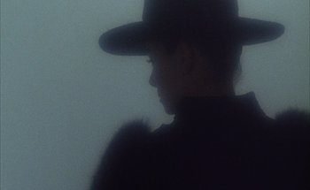 Movie still from “F for Fake” (1973), directed by François Reichenbach – A person wearing a black hat and a black coat; Close Up shot, Low angle