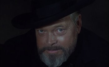 Movie still from “F for Fake” (1973), directed by François Reichenbach – A man with a beard wearing a black hat; Close Up shot, Over the shoulder angle