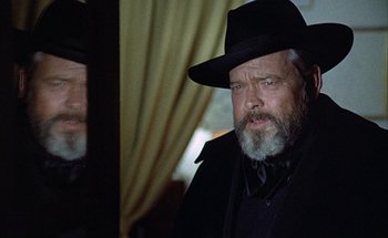 Movie still from “F for Fake” (1973), directed by François Reichenbach – A man with a beard wearing a black hat; Close Up shot, Over the shoulder angle