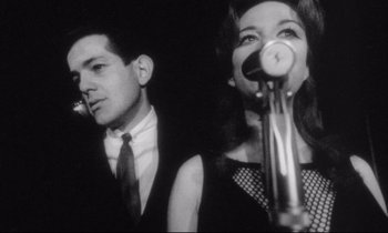 Movie still from “Faces” (1968), directed by John Cassavetes – A man and a woman standing next to each other in front of microphones; Close Up shot, Low angle