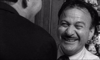 Movie still from “Faces” (1968), directed by John Cassavetes – A man in a suit and tie smiling for the camera; Close Up shot, Over the shoulder angle