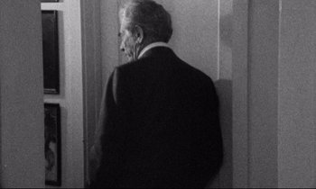 Movie still from “Faces” (1968), directed by John Cassavetes – An older man wearing a suit standing in front of a wall; Medium shot, Over the shoulder angle