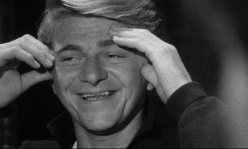 Movie still from “Faces” (1968), directed by John Cassavetes – Black and white photograph of a man smiling with one hand up to his forehead; Close Up shot, High angle