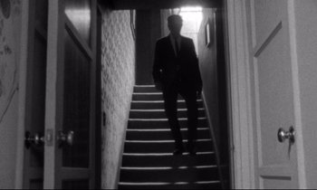 Movie still from “Faces” (1968), directed by John Cassavetes – A man in a suit walking down a set of stairs; Wide shot, Low angle
