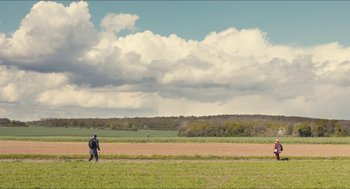 Movie still from “Faces Places” (2017), directed by Agnès Varda – A man walking across a lush green grass covered field; Extreme Wide shot, Low angle