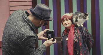 Movie still from “Faces Places” (2017), directed by Agnès Varda – A man taking a picture of a woman with a hat on; Medium shot, Low angle