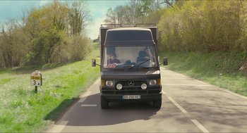 Movie still from “Faces Places” (2017), directed by Agnès Varda – A truck driving down a road near some trees; Wide shot, Low angle