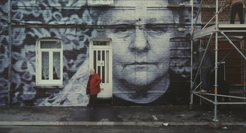 Movie still from “Faces Places” (2017), directed by Agnès Varda – A woman in a red jacket standing in front of a building; Wide shot, Low angle