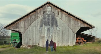 Movie still from “Faces Places” (2017), directed by Agnès Varda – Three people standing in front of a barn with a large picture of a man on it; Extreme Wide shot, Low angle