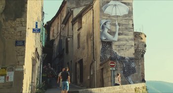 Movie still from “Faces Places” (2017), directed by Agnès Varda – A woman with an umbrella is painted on the side of a building; Extreme Wide shot, Low angle