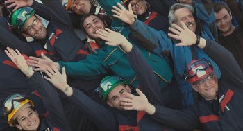 Movie still from “Faces Places” (2017), directed by Agnès Varda – A group of people standing next to each other with their hands in the air; Medium shot, Overhead angle