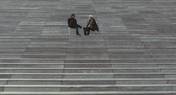 Movie still from “Faces Places” (2017), directed by Agnès Varda – Two people sitting on the steps of a building; Wide shot, High angle