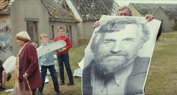 Movie still from “Faces Places” (2017), directed by Agnès Varda – A man holding up a picture of a man with a beard; Medium shot, Low angle