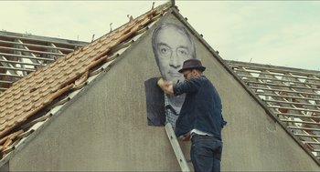 Movie still from “Faces Places” (2017), directed by Agnès Varda – A man painting a picture on the side of a building; Medium shot, Low angle