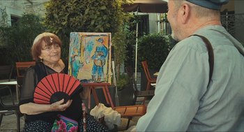 Movie still from “Faces Places” (2017), directed by Agnès Varda – A woman holding a fan in front of an easel with a painting; Medium shot, Over the shoulder angle