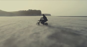 Movie still from “Faces Places” (2017), directed by Agnès Varda – A person riding a motorcycle in the middle of the ocean; Extreme Wide shot, High angle