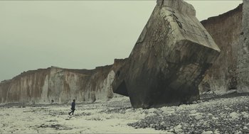 Movie still from “Faces Places” (2017), directed by Agnès Varda – A person walking on a beach next to a large rock; Extreme Wide shot, Low angle