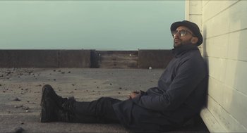 Movie still from “Faces Places” (2017), directed by Agnès Varda – A man sitting on the ground wearing a hat; Wide shot, Low angle