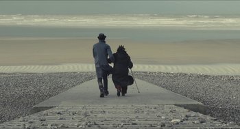 Movie still from “Faces Places” (2017), directed by Agnès Varda – A man and a woman sitting on a pier looking out at the ocean; Wide shot, High angle