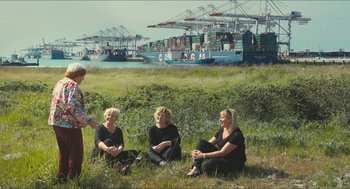 Movie still from “Faces Places” (2017), directed by Agnès Varda – A group of women sitting on the grass in front of a harbor; Wide shot, Over the shoulder angle