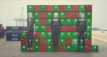Movie still from “Faces Places” (2017), directed by Agnès Varda – A wall of green and red shipping containers with pictures on them; Wide shot, Overhead angle
