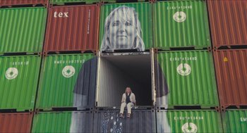 Movie still from “Faces Places” (2017), directed by Agnès Varda – A person sitting in a container on top of a platform; Wide shot, Low angle