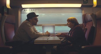 Movie still from “Faces Places” (2017), directed by Agnès Varda – A man and a woman sitting at a table with a laptop; Medium shot, Over the shoulder angle