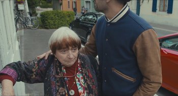 Movie still from “Faces Places” (2017), directed by Agnès Varda – An older woman and a younger man standing next to each other on the street; Close Up shot, Over the shoulder angle