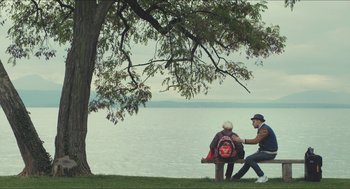 Movie still from “Faces Places” (2017), directed by Agnès Varda – Two people sitting on a park bench near a tree; Wide shot, Over the shoulder angle