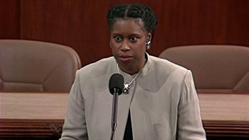 Movie still from “Fahrenheit 9/11” (2004), directed by Michael Moore – A woman is speaking in front of a microphone in a courtroom; Close Up shot, Low angle