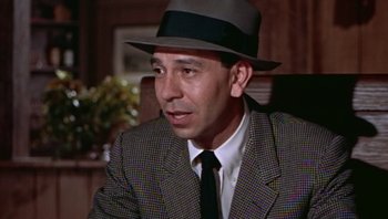 Movie still from “Fahrenheit 9/11” (2004), directed by Michael Moore – A man wearing a suit and a hat in a room; Close Up shot, High angle