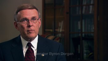 Movie still from “Fahrenheit 9/11” (2004), directed by Michael Moore – A man in a suit and tie in a room; Medium shot, Over the shoulder angle