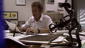 Movie still from “Fahrenheit 9/11” (2004), directed by Michael Moore – A man sitting at a table working on a laptop computer; Medium shot, High angle