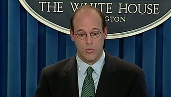 Movie still from “Fahrenheit 9/11” (2004), directed by Michael Moore – A man in a suit and tie standing in front of a sign; Close Up shot, Low angle