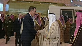 Movie still from “Fahrenheit 9/11” (2004), directed by Michael Moore – Two men shaking hands in front of a group of people; Medium shot, Over the shoulder angle