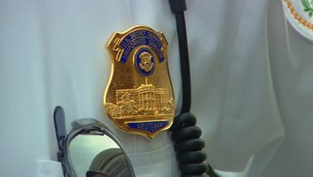 Movie still from “Fahrenheit 9/11” (2004), directed by Michael Moore – A police officer's badge is hanging on the side of a car; Close Up shot, Low angle