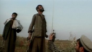 Movie still from “Fahrenheit 9/11” (2004), directed by Michael Moore – A man holding a rifle in his hand and another man holding a gun in his other hand; Medium shot, Low angle