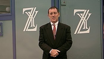 Movie still from “Fahrenheit 9/11” (2004), directed by Michael Moore – A man wearing a suit and tie standing in front of a wall; Medium shot, Low angle